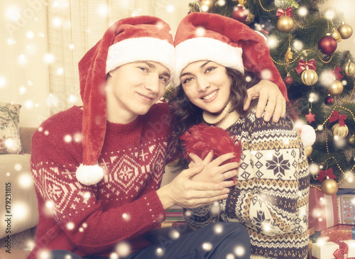 Happy couple embrace near christmas tree and decoration at home. Winter holiday and love concept. Yellow toned with snow.