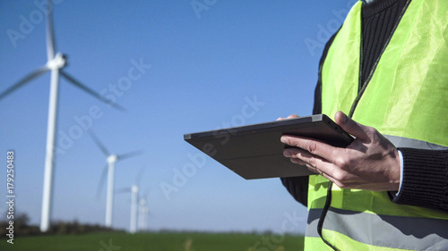 Close up view of engineer man hands working with digital tablet against wind turbine on sunny day