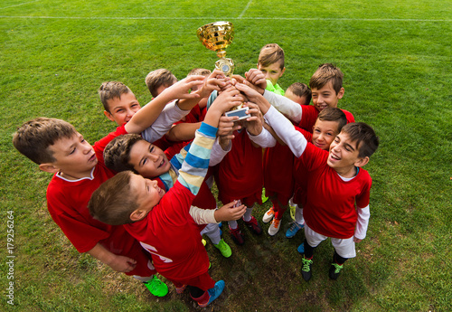 Kids soccer football -  children players celebrating with a trophy after match on soccer field photo