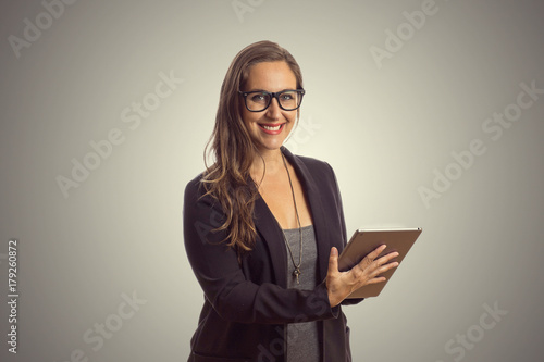 Imagem de mulher linda intelectuel de oculos em pé enquanto segura o comprimido digital em suas mãos e lendo o texto ao fundo cinza. Chefe Mulher de negócios que trabalha no escritório. photo