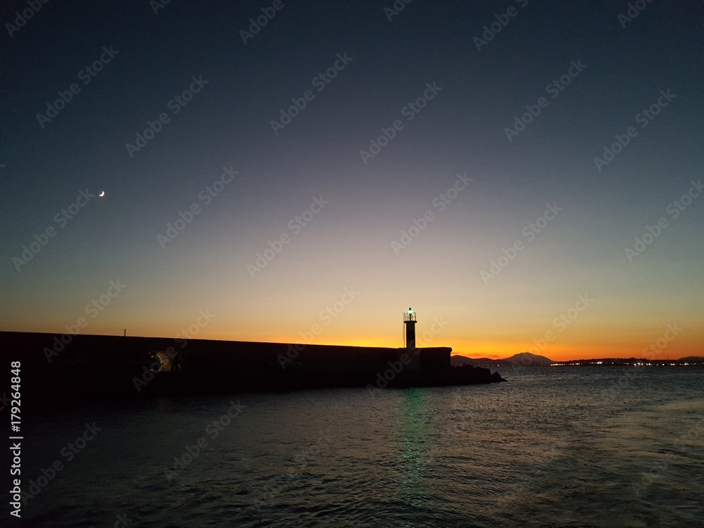 Seascape at sunset with a lighthouse and the moon