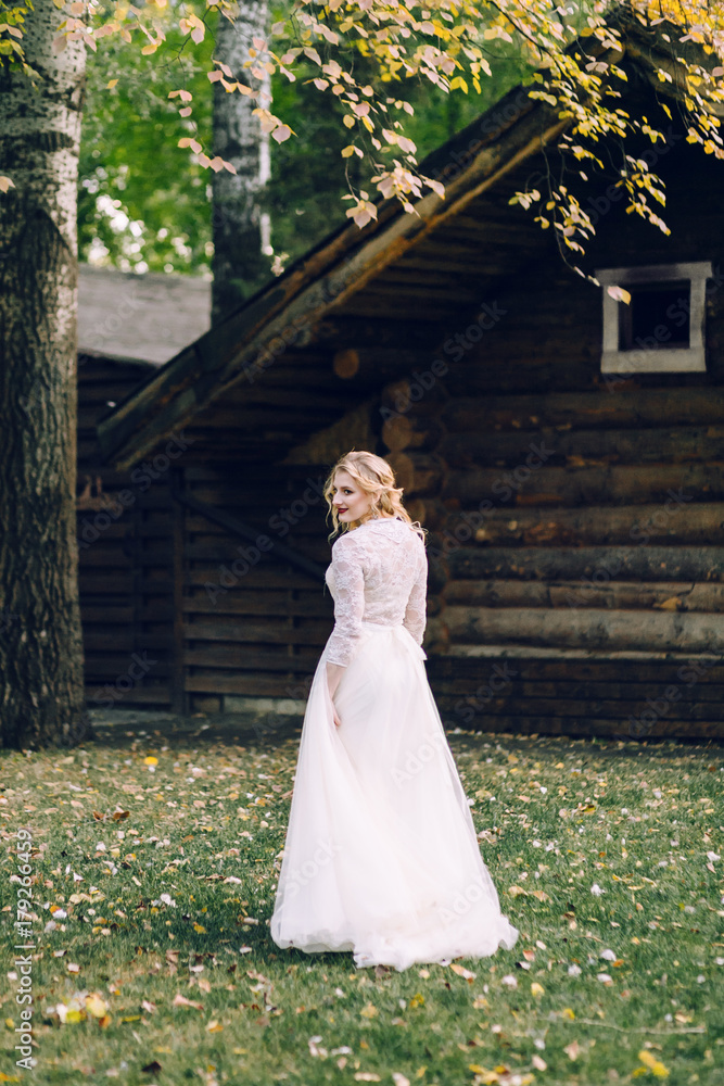 Happy bride with curly blonde hair pose next to the wooden house back. Rustic wedding