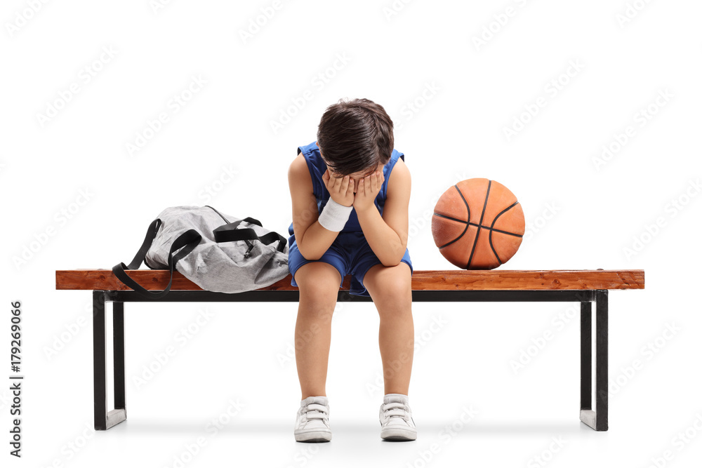 Naklejka premium Sad little basketball player sitting on a bench and crying