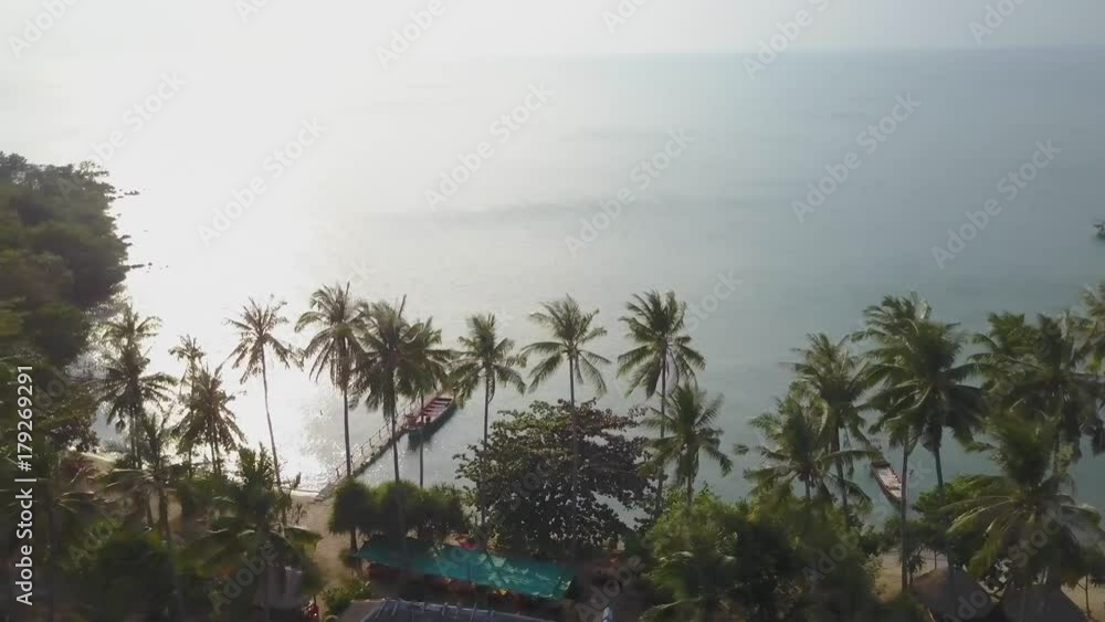 Wide shot of aerial of the Gulf of Siam looking through palms trees with the a fishing boat at a dock and light reflecting off of the water. Wide shot of aerial of the Gulf of Siam looking through palms trees with the a fishing boat at a dock and light reflecting off of the water.