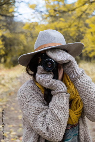 GIrl in gray hat taking pictures with a professional camera at the autumn park