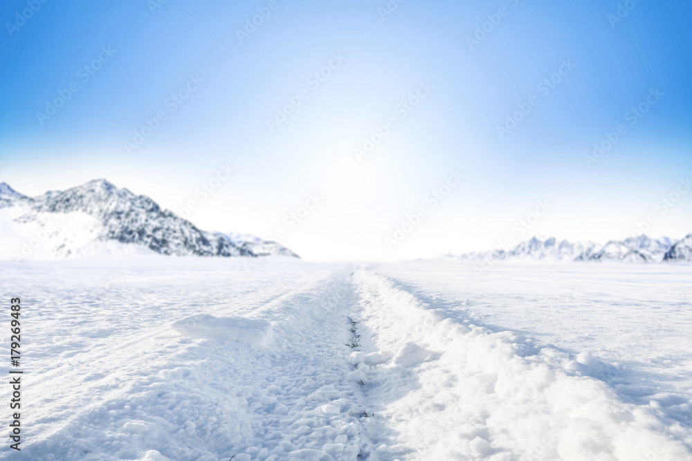 Winter Background of foreground of road covered with snow and ice. In the background, the arctic landscape of the mountains with the beautiful blue sky.