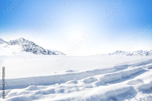 Winter Background of foreground of road covered with snow and ice. In the background, the arctic landscape of the mountains with the beautiful blue sky. © magdal3na
