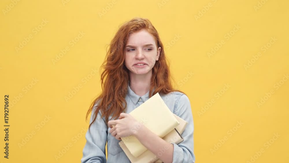 Tired ginger woman in denim shirt holding books and yawns over yellow background Tired ginger woman in denim shirt holding books and yawns over yellow background