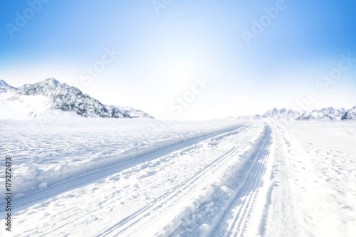 Winter Background of foreground of road covered with snow and ice. In the background, the arctic landscape of the mountains with the beautiful blue sky.