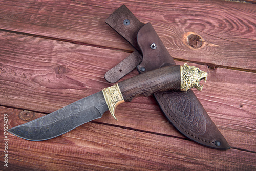 Hunting knife with leather case on the background of wood texture