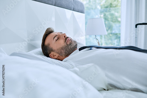 Elegant man taking nap in hotel room bed after business trip