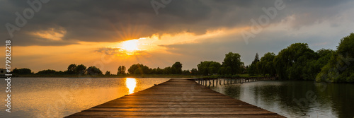 Wooden pier, bridge over lake at dramatic sunset with stormy clouds. Kuchyna, Slovakia. Panorama 3:1 photo