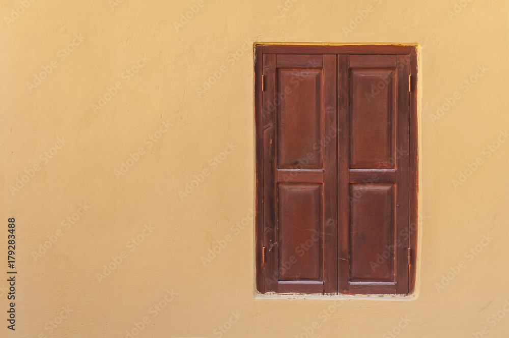 Close view of modern closed dark red wooden window on yellow cement textured house wall