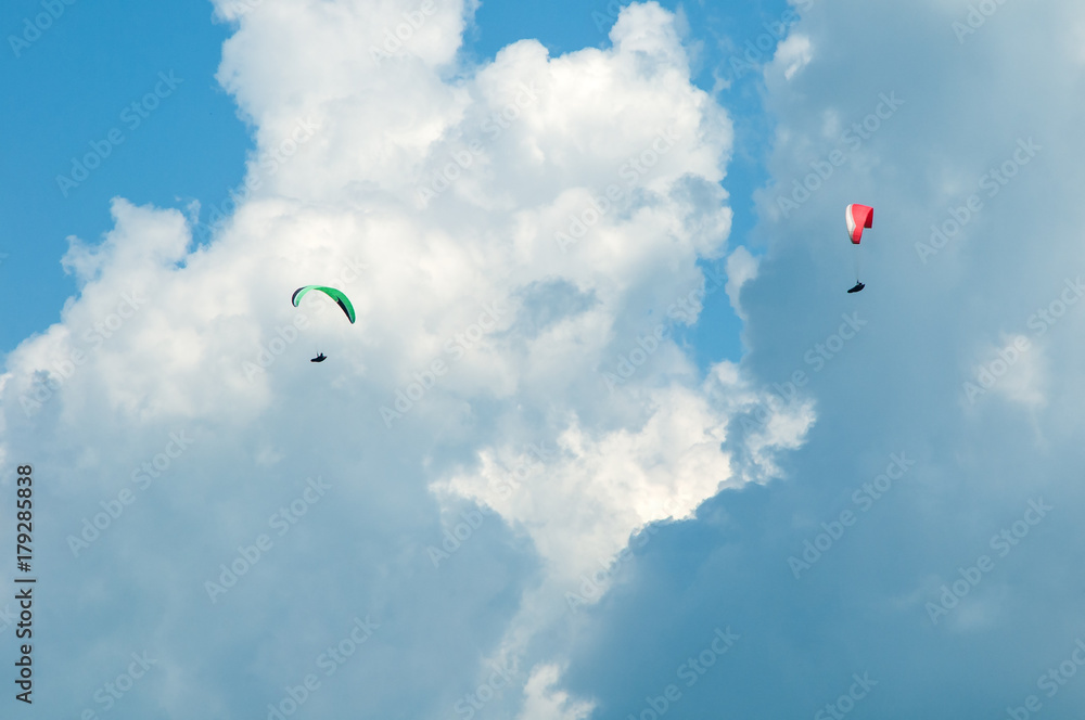 Two paragliders flying in the blue sky against the background of clouds. Paragliding in the sky on a sunny day. Two paragliders flying in the blue sky against the background of clouds. Paragliding in the sky on a sunny day.