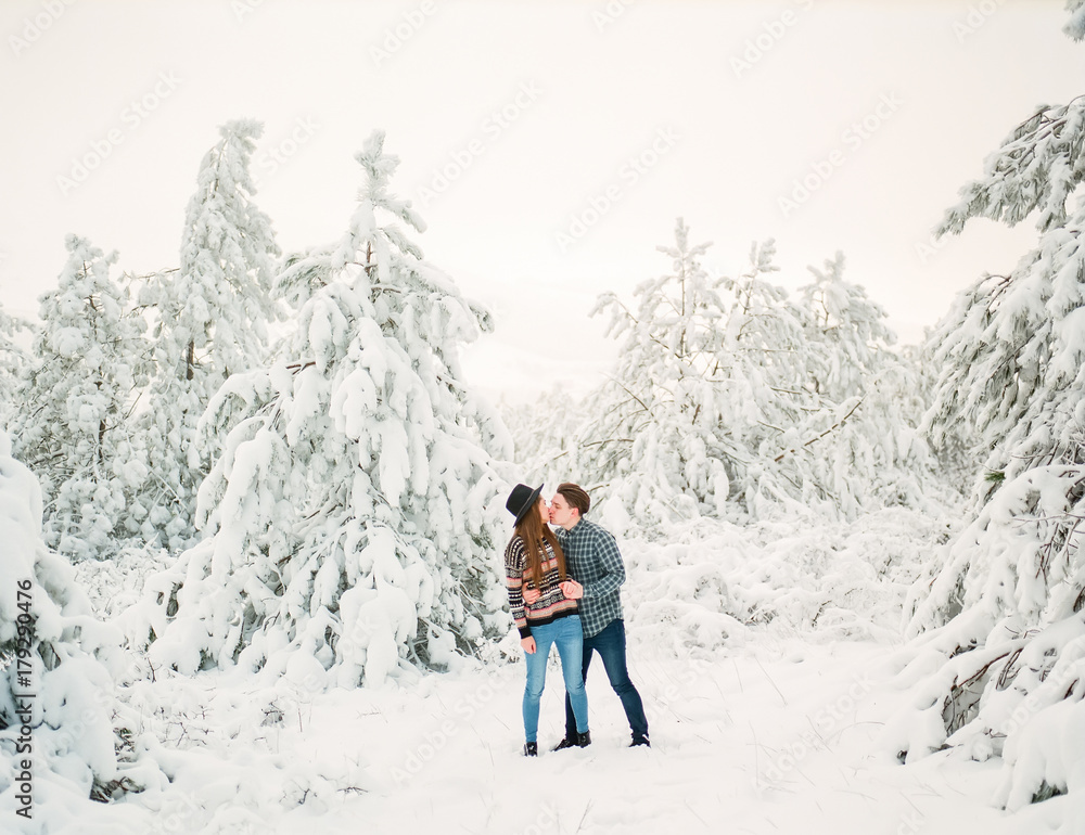 Happy young couple kissing in winter forest. Winter Christmas story.