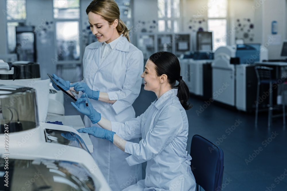 Fototapeta premium Relationships with colleagues. Happy positive nice women talking to each other and discussing work while working in the lab