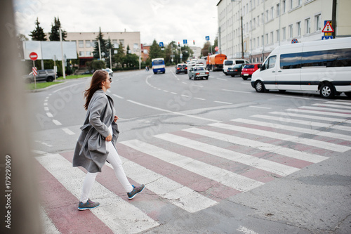 Girl in gray coat with sunglasses and handbag walking on the pedestrian crossing.