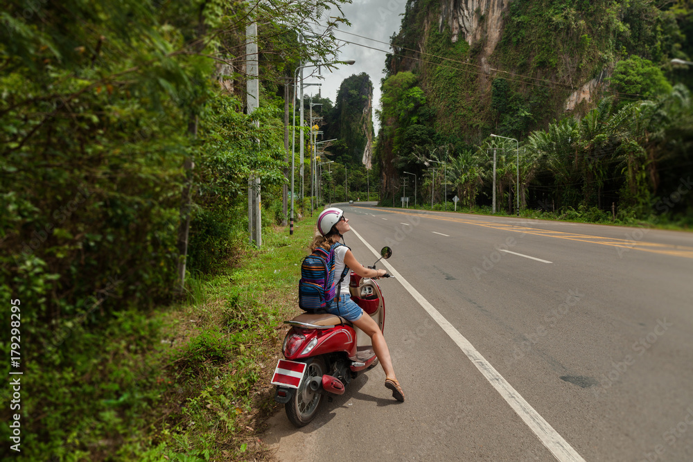 tourist woman sitting on classic scooter against the background of the mountains of Krabi Province, Thailand. tourist woman sitting on classic scooter against the background of the mountains of Krabi Province, Thailand.