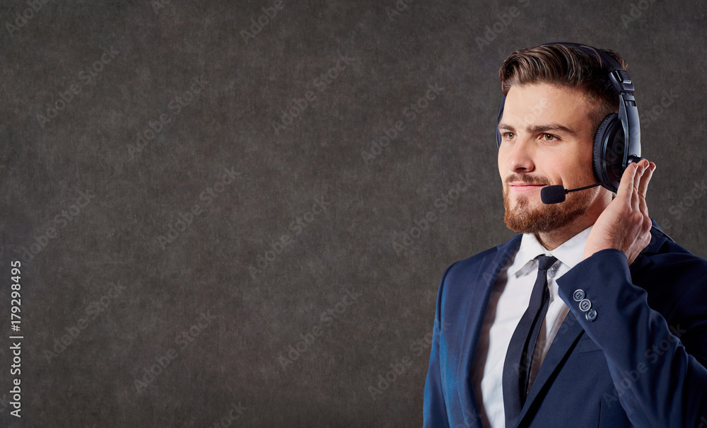 Naklejka premium A male call center operator with headset on his head answers calls on the office background.