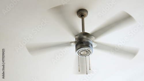 Ceiling fan is rotating at the ceiling of the room. Electric climate equipment.