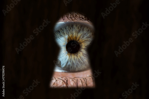 Female blue eye looking through the keyhole. Concept of voyeurism, curiosity, Stalker, surveillance and security photo