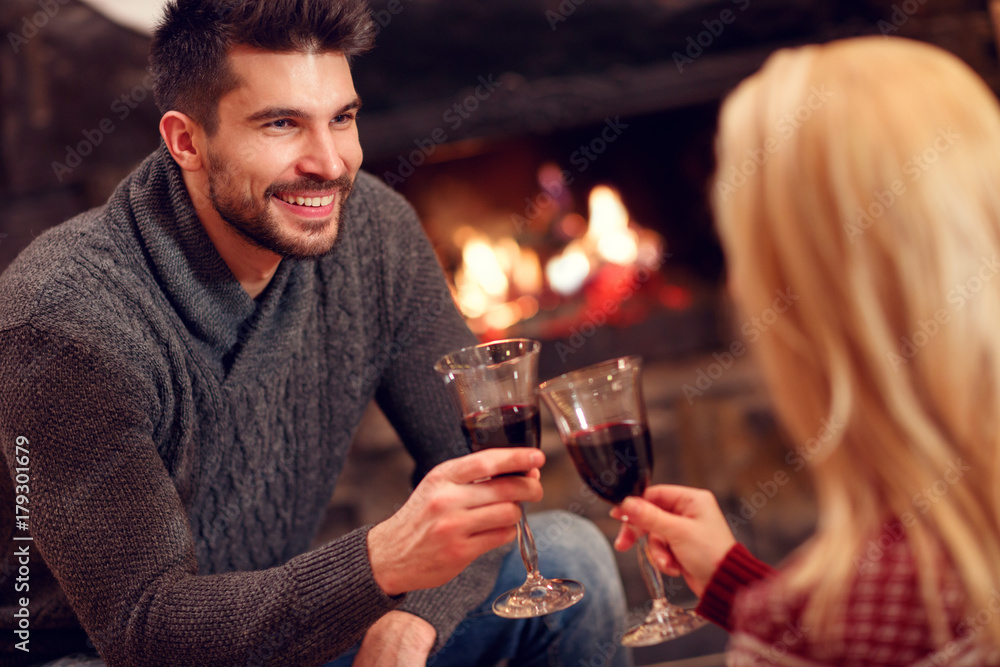 romantic couple sitting on floor at burning fireplace and drink wine.