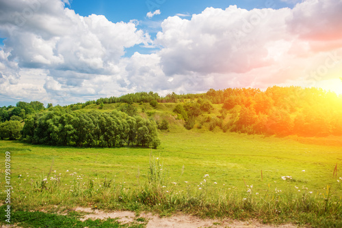 Green grass field on small hills and blue sky with clouds photo