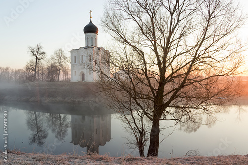 A misty lake with a boat in front of the church in the early spring at dawn