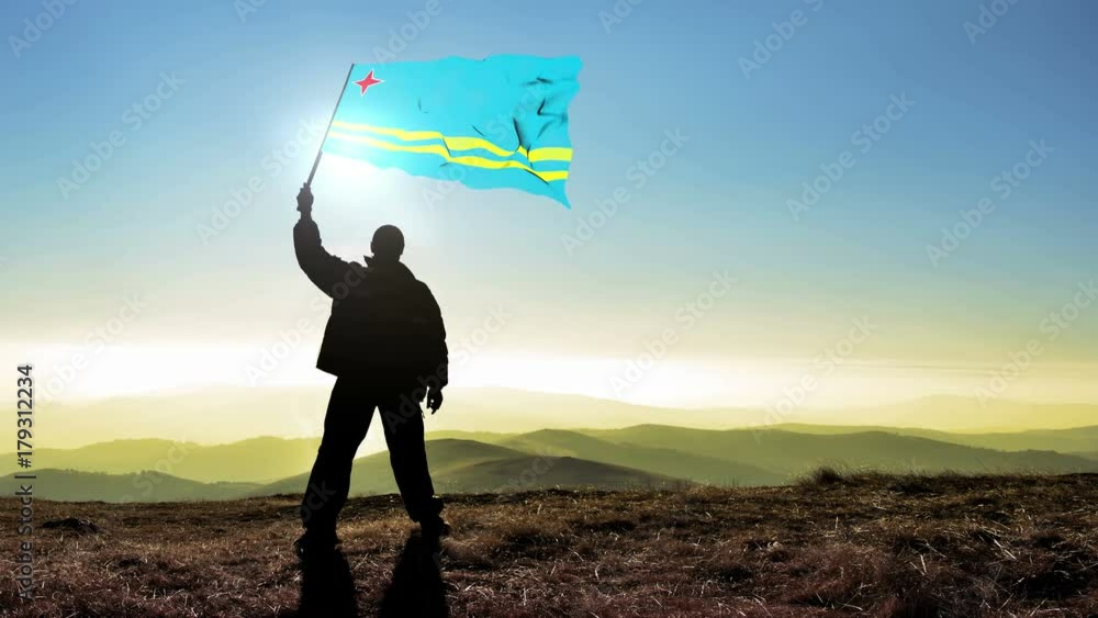 Successful silhouette man winner waving Aruba flag on top of the mountain peak. Cinemagraph LOOP background