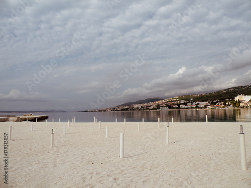 interesting beach with white sand and white stands for umbrellas, in the background Mediterranean city of Crikvenica, Croatia photo