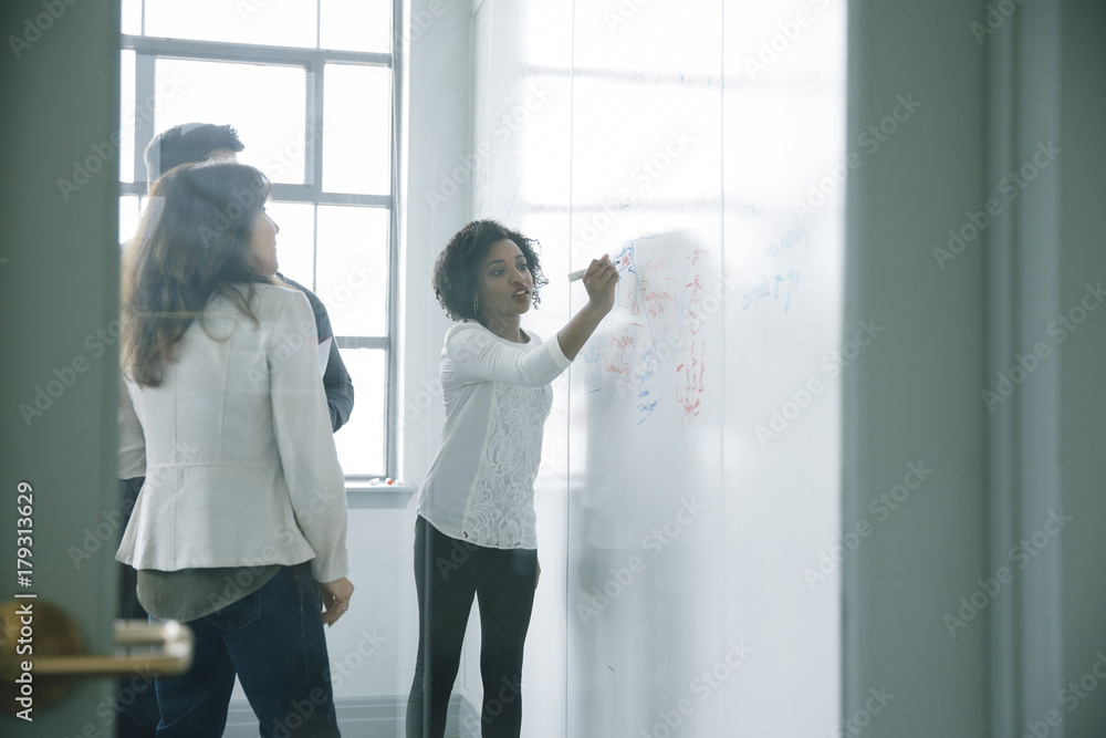 © John Fedele/Blend Images - Businesswoman writing on whiteboard in meeting