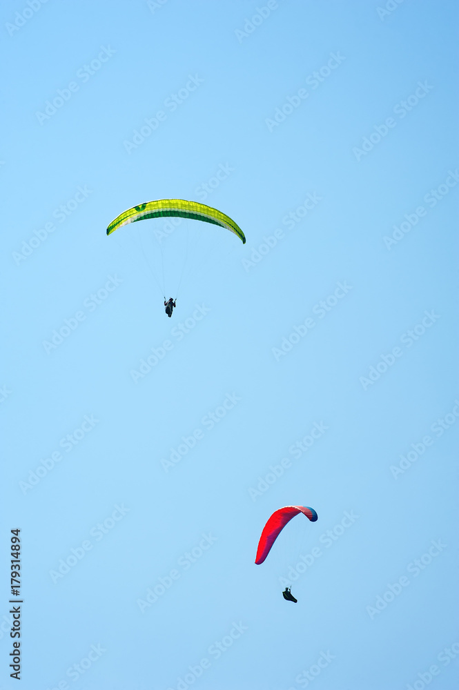 Vertical photo of two paragliders flying in the blue sky. Paragliding in the sky on a sunny day. Vertical photo of two paragliders flying in the blue sky. Paragliding in the sky on a sunny day.