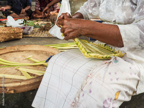 Slika na platnu Old woman making bamboo baskets called canang sari in a local temple in Ubud for