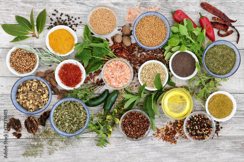 Spice and herb seasoning with fresh and dried herbs and spices, including chili pepper selection, mustard powder and seeds, ground and whole peppercorns and olive oil on rustic wood. Top view.