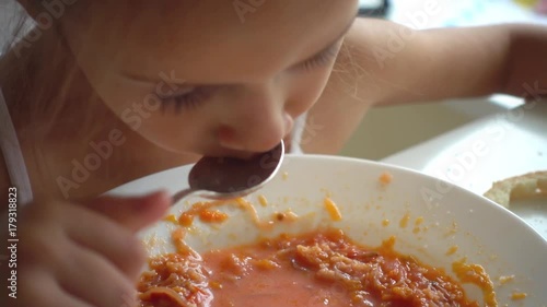 Portrait of a little girl who eats soup, slow motion. Slow motion shooting of 100 fps a child is eating vegetable soup.
 photo
