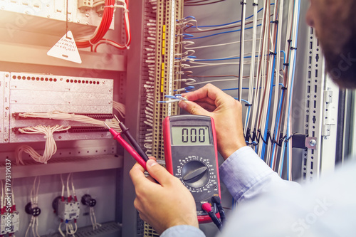 Obraz na płótnie Engineer tests industrial electrical cabinet. Wire in hand of electrician with multimeter. Professional in control panel of industrial equipment. w salonie