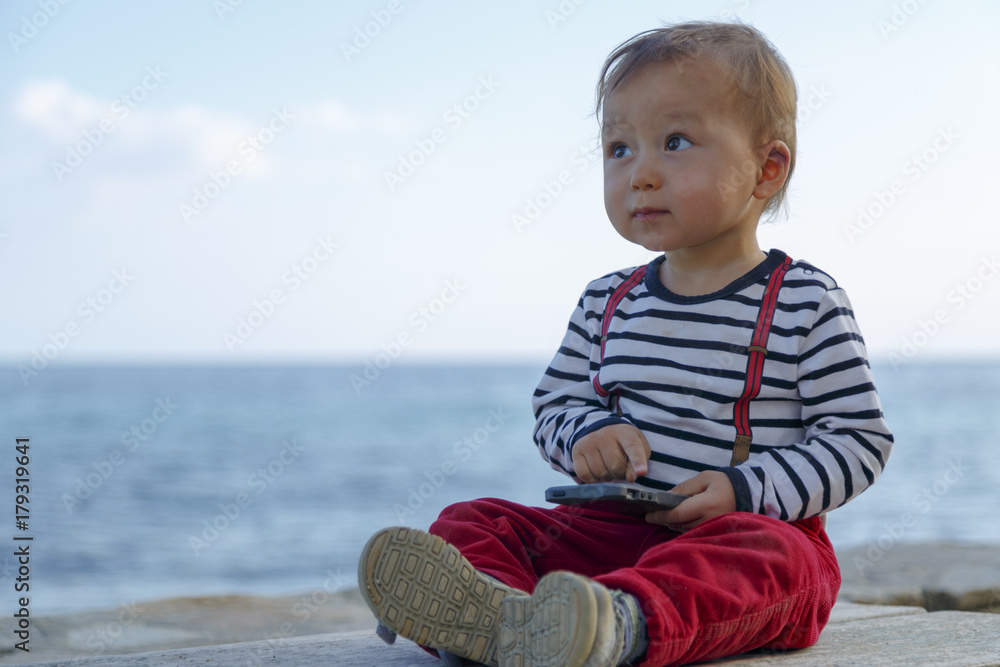 A baby boy is playing with mobile phone on a beach A baby boy is playing with mobile phone on a beach