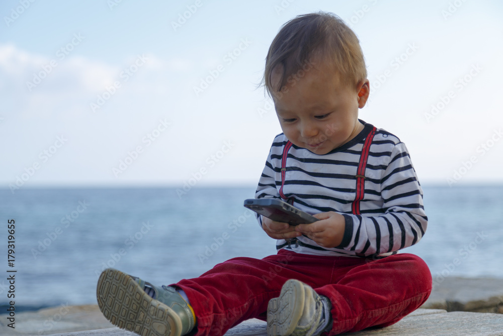 A baby boy is playing with mobile phone on a beach A baby boy is playing with mobile phone on a beach