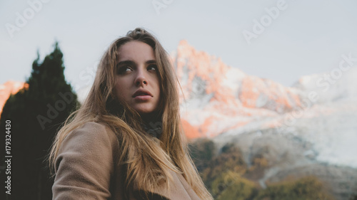 Beautiful Cacasian female wearing brown coat posing against Mont Blanc massif during sunset