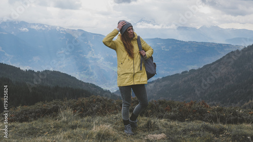 Hipster young girl with backpack hiking in mountains. Tourist traveler walking on top of the mountain