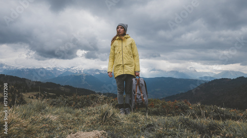 Hipster young girl with backpack hiking in mountains. Tourist traveler walking on top of the mountain