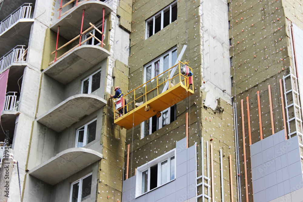 worker in yellow front suspended cradle on a newly built high-rise building