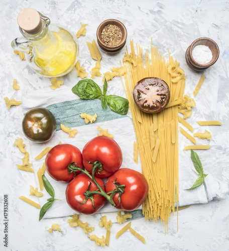 preparation of appetizing Italian pasta, with tomatoes, basil, and oil in a decanter, spices and seasonings on a white rustic background, top view