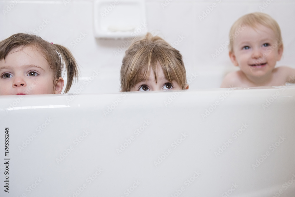 Caucasian boy and girls peaking from bathtub Caucasian boy and girls peaking from bathtub