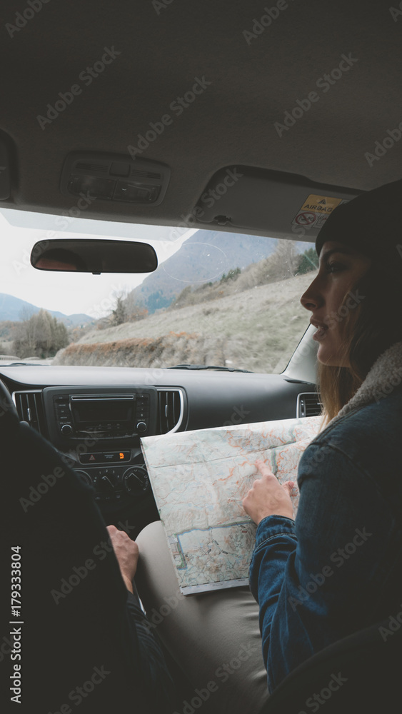 Fototapeta premium Rear view shot of couple traveling by car. Woman holding map, laughing and smiling. Couple on a road trip.
