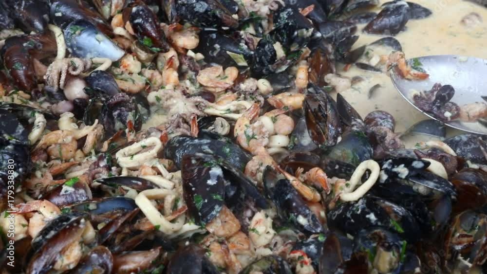 Close up of cooking fresh seafood, shrimps, mussels, calamari and octopus in white sauce in big frying pan, close up, high angle view Close up of cooking fresh seafood, shrimps, mussels, calamari and octopus in white sauce in big frying pan, close up, high angle view