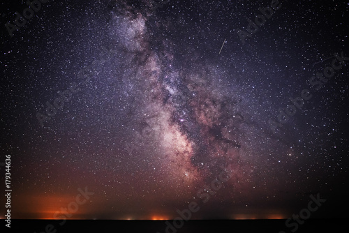 Background of bright and night-starry sky with the Milky Way upon on it and light over the water