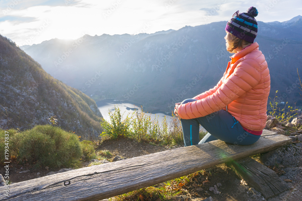 Young woman sitting on the branch on the viewpoint, relaxing after hiking and watching the Bohinj Lake, Slovenia