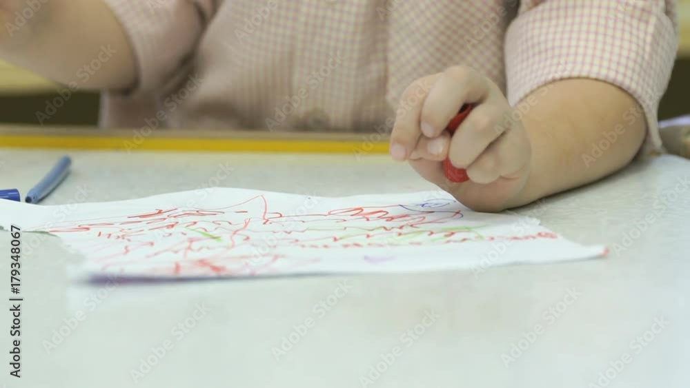 Close-up of unknown little child draws and paints pictures with felt-tip sitting at desk in the kindergarten Close-up of unknown little child draws and paints pictures with felt-tip sitting at desk in the kindergarten