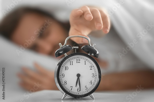 Young man switching off alarm clock signal while lying in bed at home